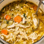 Steaming bowl of classic chicken soup with visible chicken and vegetables.